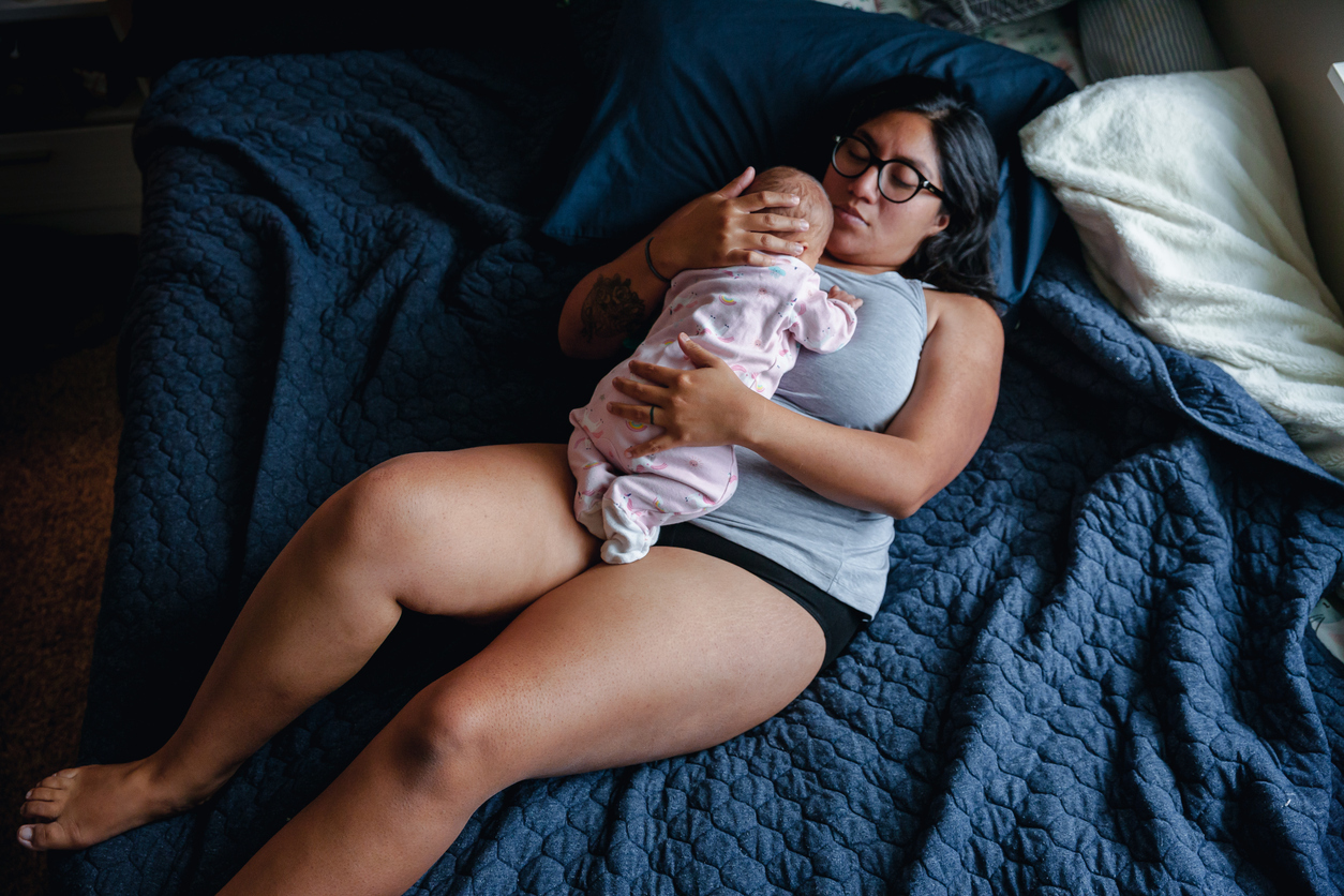 Woman lying on bed with newborn on stomach
