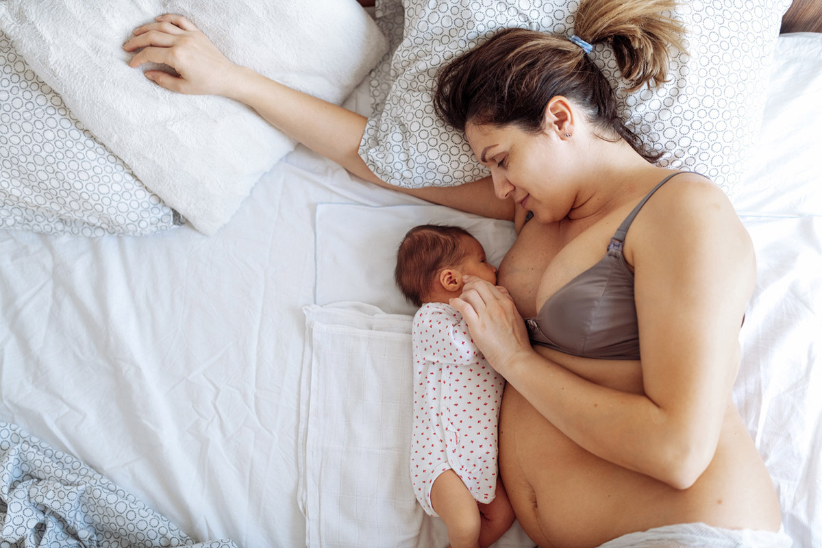 New mom wearing postpartum mesh underwear while breastfeeding her newborn baby lying down in a bed.