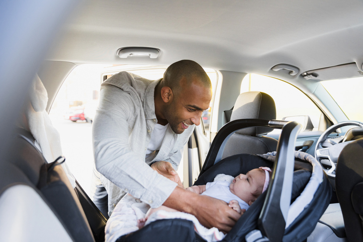 Black father smiling while buckling in mixed race child in a rear-facing car seat