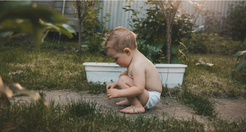 shirtless toddler boy playing on a dirt path outdoors