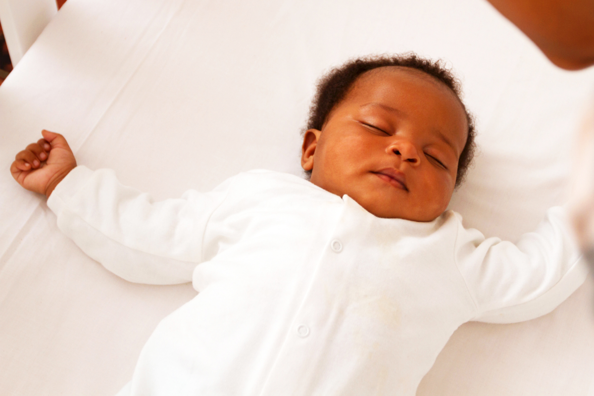 Black baby sleeping on their back in a crib safe sleep environment with their parent looking at them.