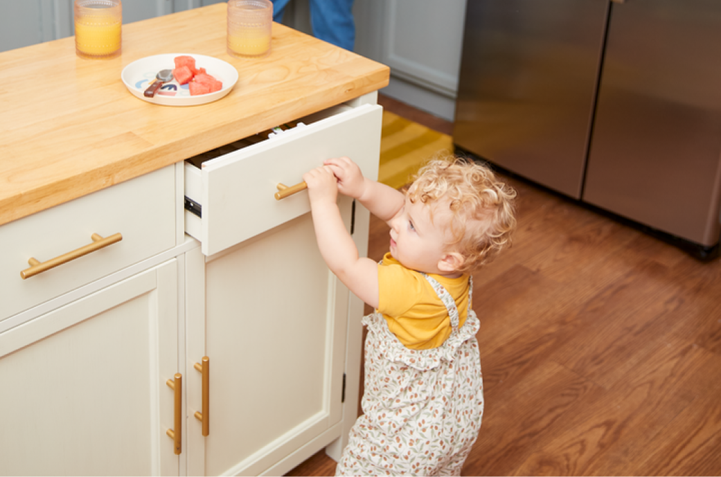 young toddler getting into a kitchen drawer, but is interrupted by a drawer lock