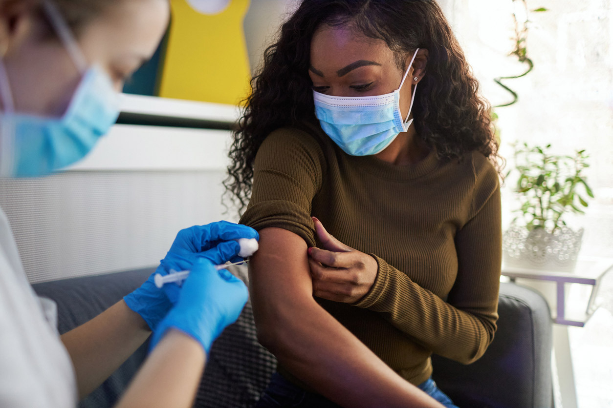 Woman wearing a protective face mask while a female nurse administers a vaccine into the woman's upper arm. 