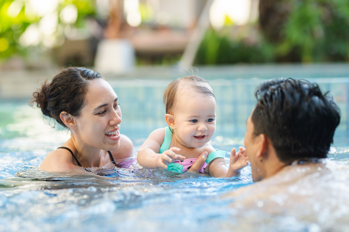 Parents holding baby swimming in pool smiling and laughing