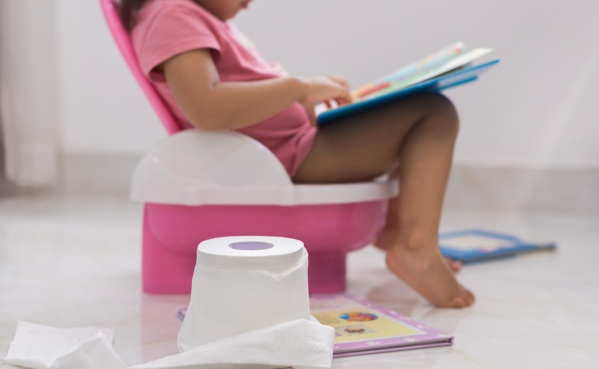 Little girl on pink potty, reading a book